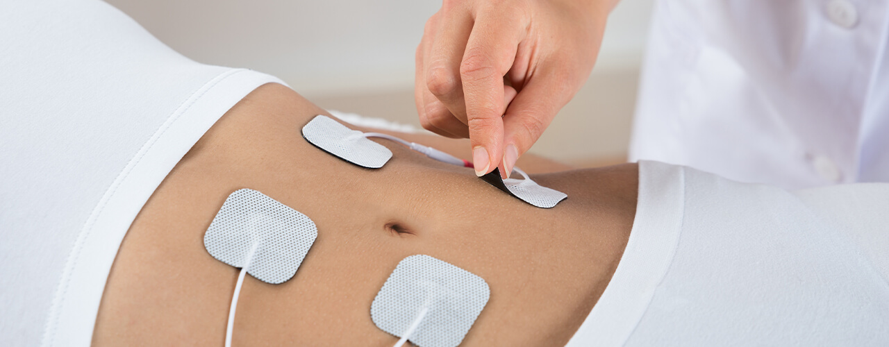 Female patient lying on her back while physical therapist applies the electrodes as part of electrical stimulation therapy for pain relief.